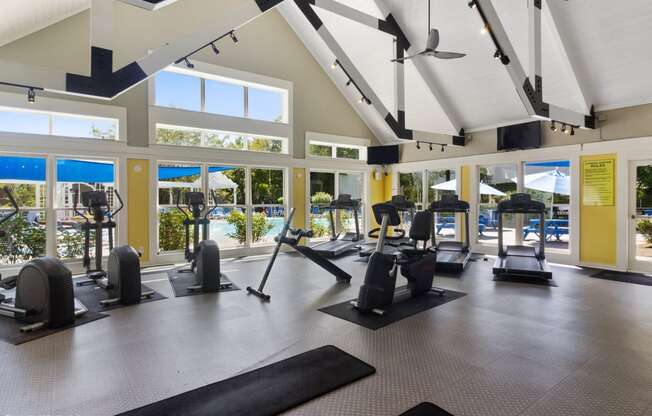 a gym with exercise equipment and windows with a pool in the background