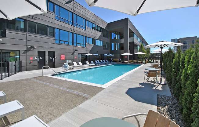 a swimming pool with lounge chairs and umbrellas in front of a building