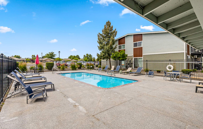 A pool area with sun loungers and a building in the background.