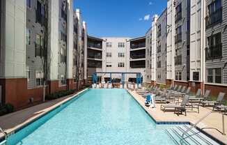 a swimming pool with lounge chairs in front of an apartment building