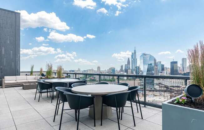 A table with chairs is set up on a rooftop terrace with a city skyline in the background