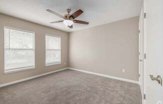 A room with a ceiling fan and two windows.