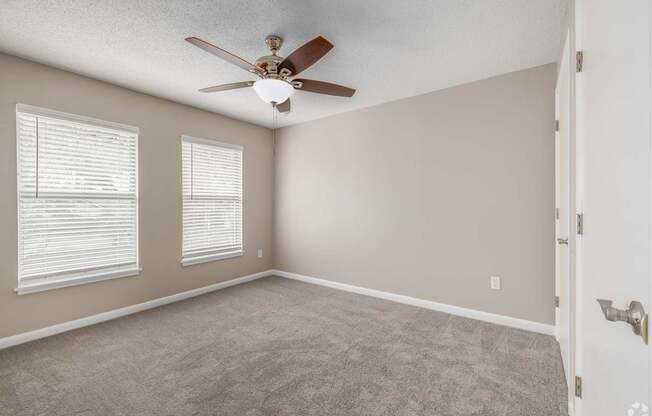 A room with a ceiling fan and two windows.