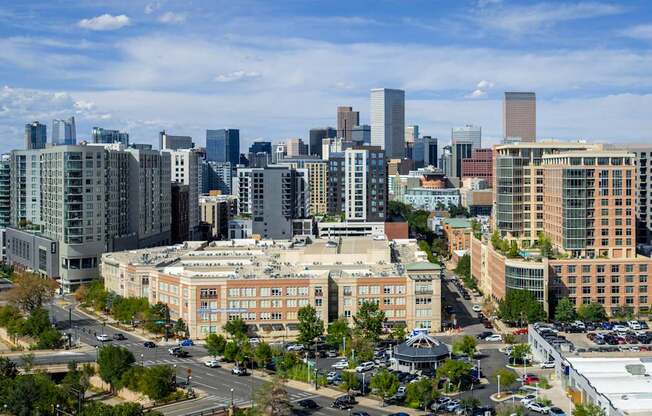 A cityscape with a mix of modern and older buildings, a clear sky, and a busy road with vehicles.