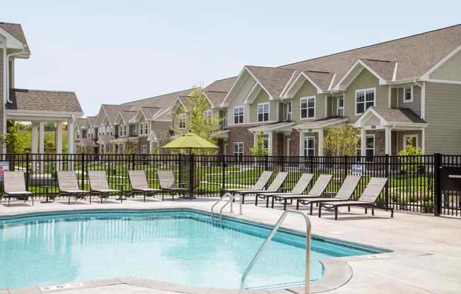 A pool surrounded by lounge chairs and a fence in front of a row of houses.