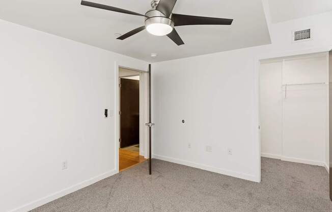 A room with a ceiling fan and a door leading to another room.