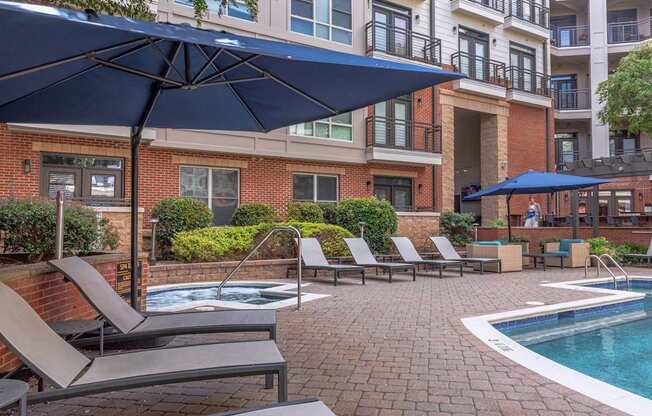A pool area with lounge chairs and umbrellas in front of a brick building.