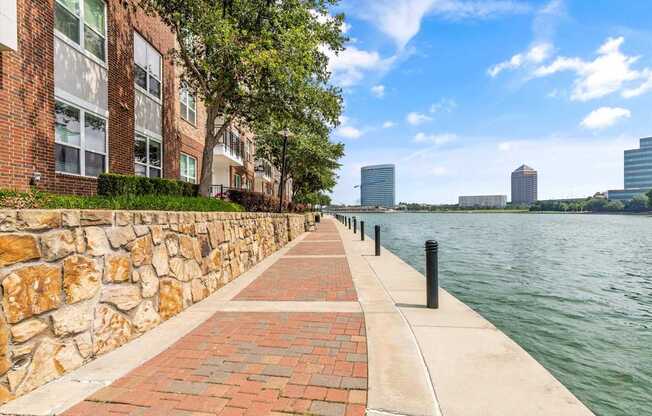 A walkway next to a body of water with a stone wall on one side and buildings in the distance.