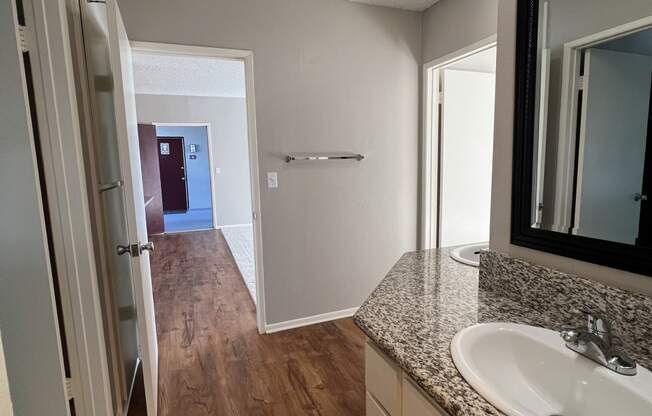 a bathroom with a sink and mirror and a hallway with a door to a bedroom