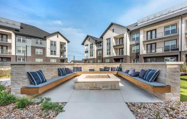 A modern outdoor seating area with benches and a fire pit in front of apartment buildings.