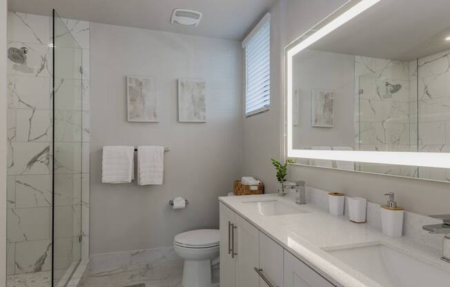 A bathroom with a marble shower, white toilet, and a white sink.