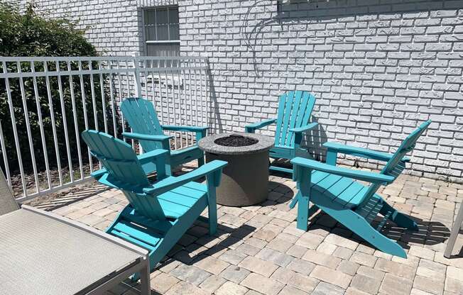 a patio with blue adirondack chairs and a fire pit