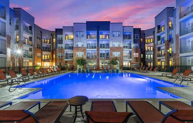 a swimming pool at night with an apartment building in the background
