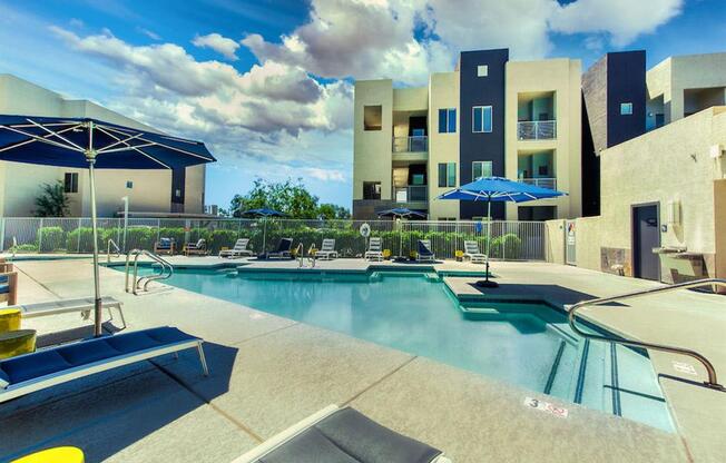 The Craft at Gilbert and Baseline Pool with buildings in the background and patio umbrella up front. Four lounge chairs line the pool.