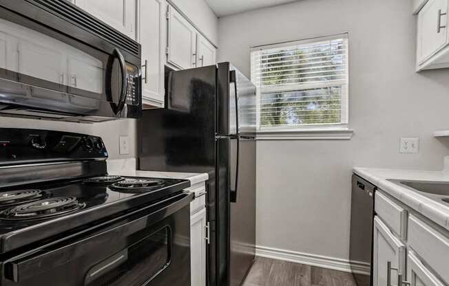 A black refrigerator in a kitchen with white cabinets.