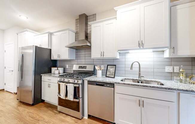 A modern kitchen with a stainless steel refrigerator, a stove with a cooking pot on it, and a sink with a faucet.