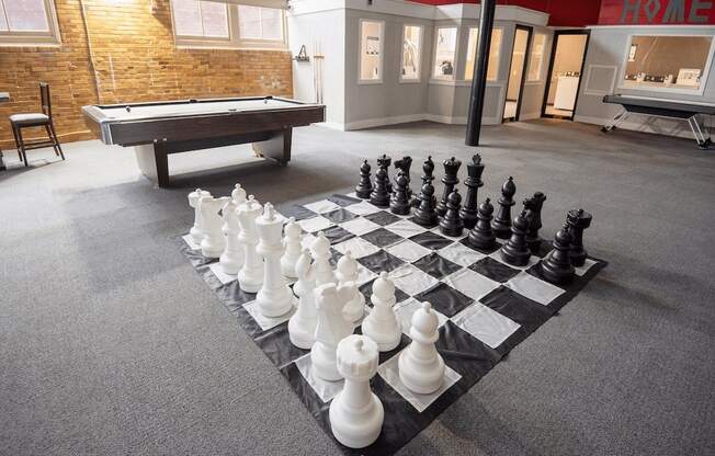 A chess board with pieces set up on a carpet in a room with a pool table and a brick wall.