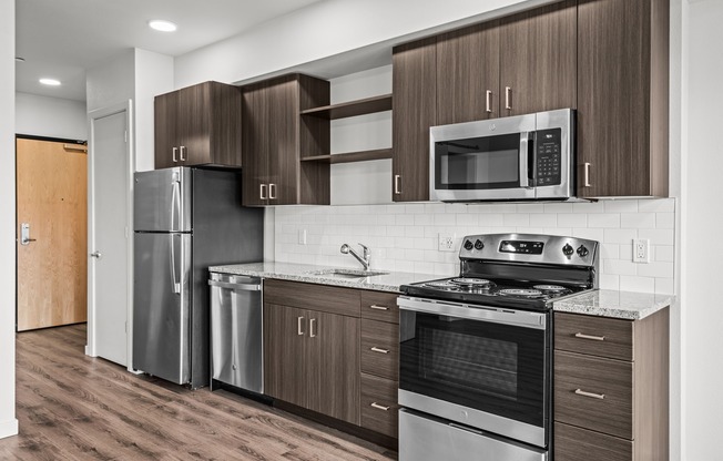 Studio kitchen with stainless-steel dishwasher, oven, range, microwave, and refrigerator, granite countertops and white subway-style backsplash.