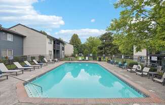 A swimming pool surrounded by lounge chairs and trees.