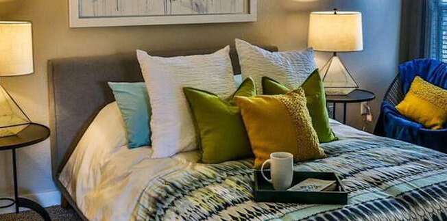 A bedroom with a bed, a chair, and two lamps.