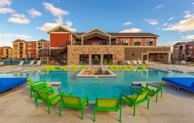A resort-style outdoor pool here at The Park featuring bright green lounge chairs, clear blue water, and a modern clubhouse backdrop, creating a vibrant, inviting space perfect for relaxing and socializing.
