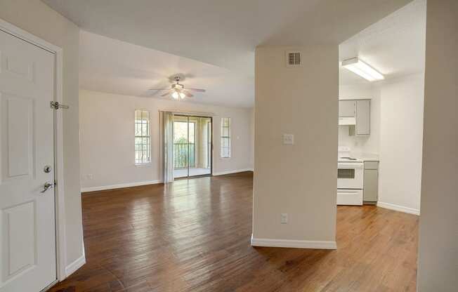 an empty living room and kitchen with wood floors and a ceiling fan