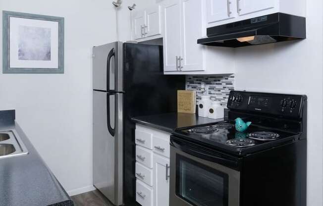 Fifteen 50 apartments Las Vegas kitchen with black and silver appliances, white cabinets, and modern black countertops and greyscale tile backsplash