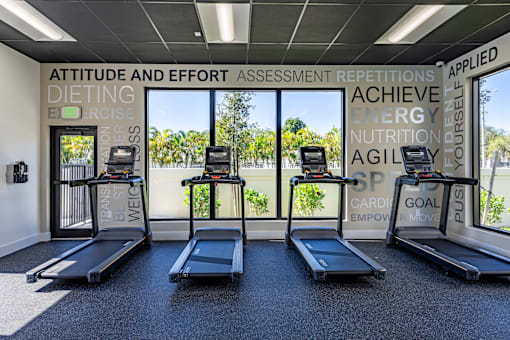 a gym with treadmills and windows with a tennis court in the background the gym  at a residential apartment community Resia in Decatur GA