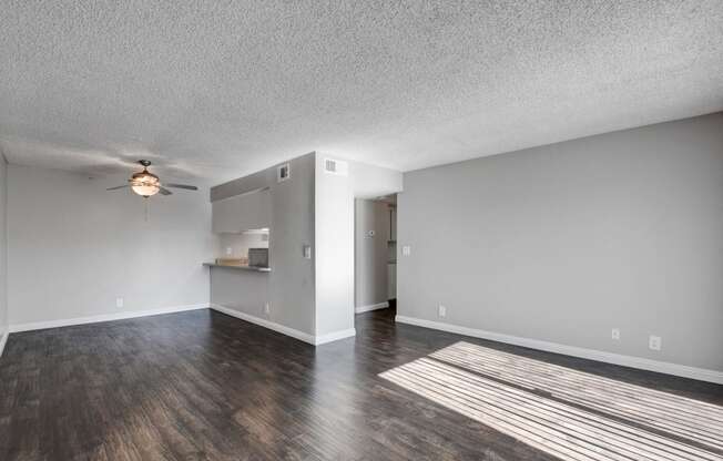 the living room and kitchen of an empty apartment with wood floors and a ceiling fan