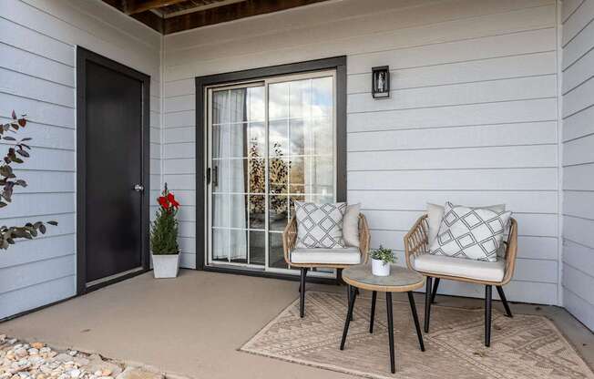 A patio with two chairs and a table with a potted plant and a door.