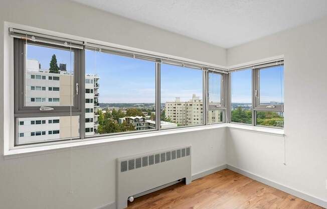 an empty room with windows and a radiator and a city view