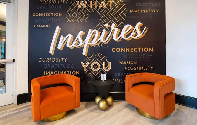 Two orange chairs are in front of a black wall with words that inspire.