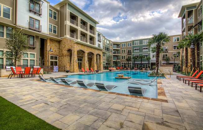 an outdoor swimming pool with lounge chairs and trees in front of an apartment building