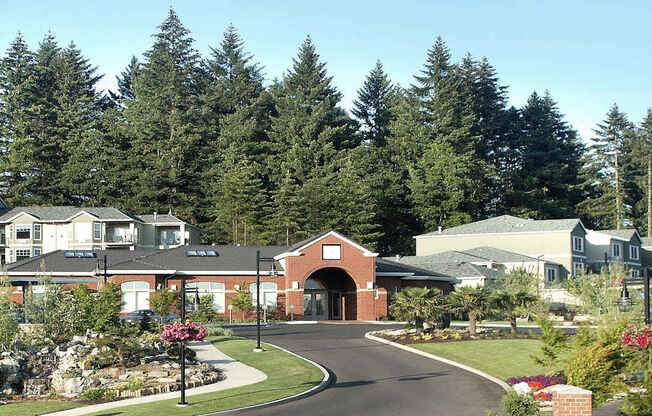 A large building with a red brick entrance sits in front of a forest of tall trees at Wilsonville Summit Apartments, Wilsonville , OR, 97070