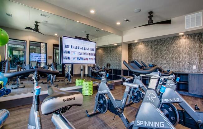 a gym with cardio bikes and a large screen