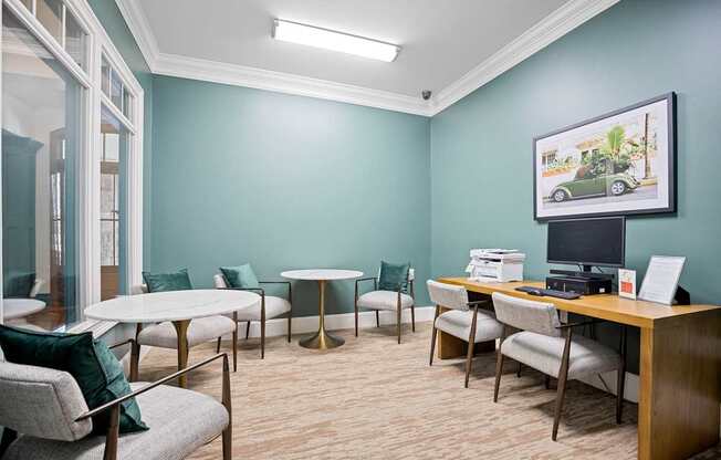 A room with a desk, chairs, and a framed picture of a car on the wall.