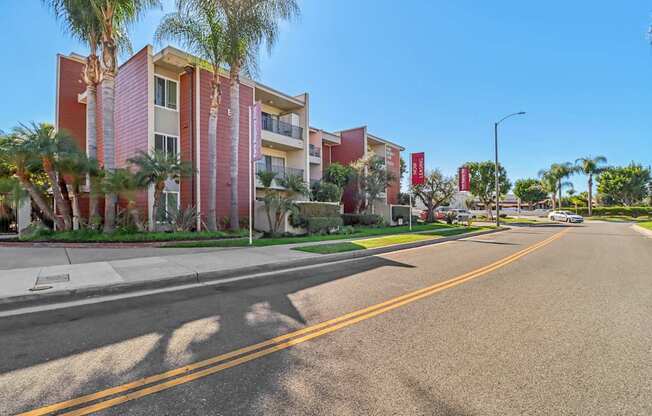 A street view of a residential area with apartment buildings and palm trees.
