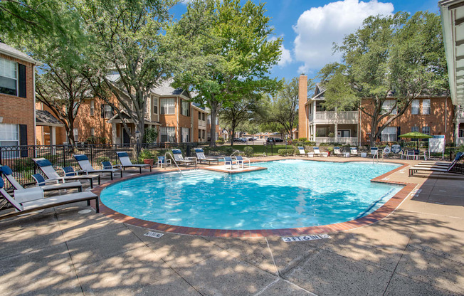 A pool surrounded by trees and chairs in a sunny day.