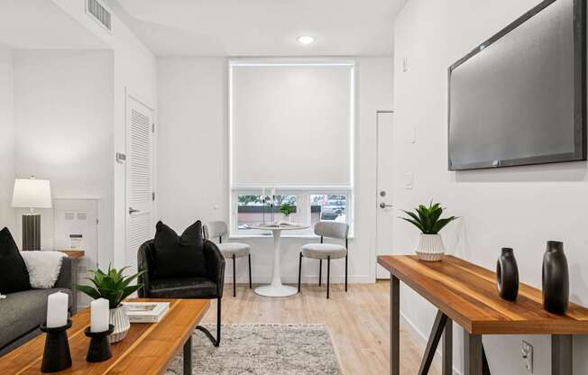 A modern living room with a grey couch, a black chair, a wooden table, and a flat-screen TV mounted on the wall.