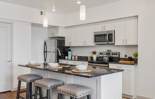 a kitchen with white cabinets and a counter top with three stools