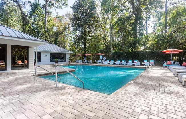 A pool surrounded by trees and chairs.