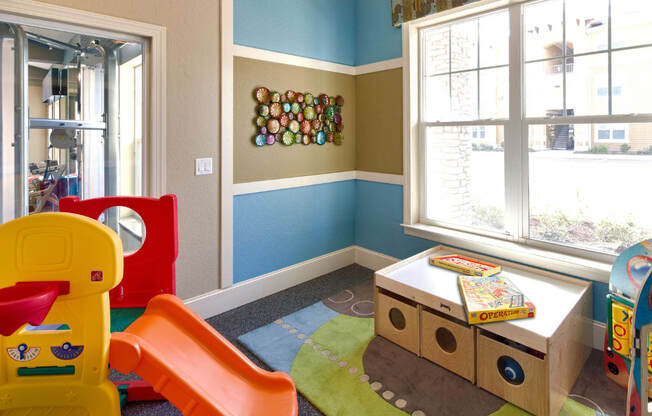 A child's playroom with a yellow chair, a red slide, and a brown and green play mat.