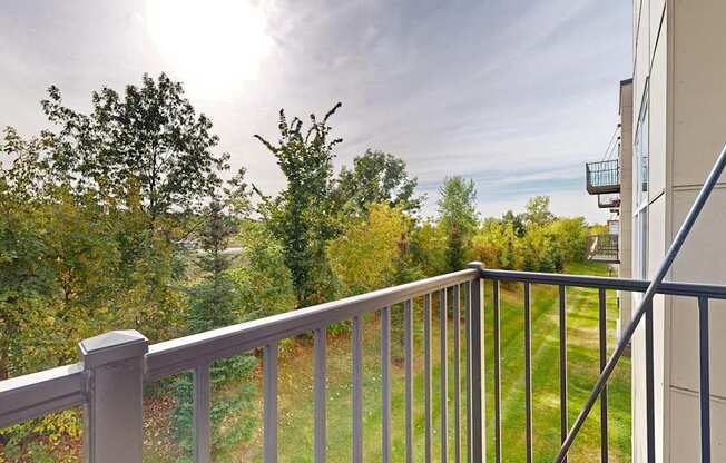A balcony with a metal railing overlooks a green landscape.