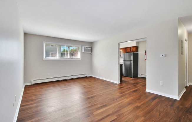 an empty living room with wood flooring and a kitchen