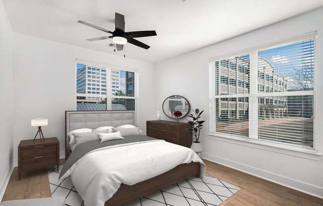A bedroom with a large bed, a ceiling fan, and a view of a cityscape through the window.