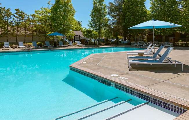A swimming pool with a blue umbrella and lounge chairs.