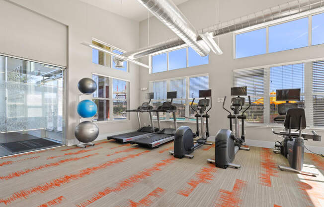 a gym with weights and exercise equipment in a building with large windows at Ridge at Thornton Station Apartments, Thornton, CO