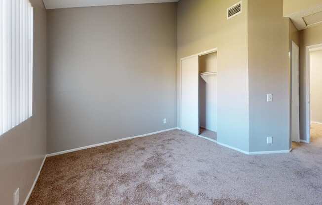 Ontario Apartments - Rancho Vista - Unfurnished Bedroom With Carpet Flooring, a Window With Shutters, and a Closet in the Corner