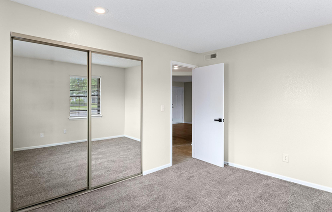 Gold carpeted bedroom interior and mirrored closet at The Arbor Apartments in Blue Springs, Missouri