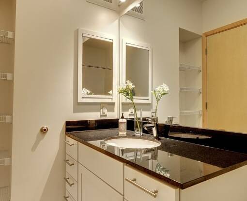 Bathroom in Flat J at Coze Flats with white cabinets, mirror and black granite countertops